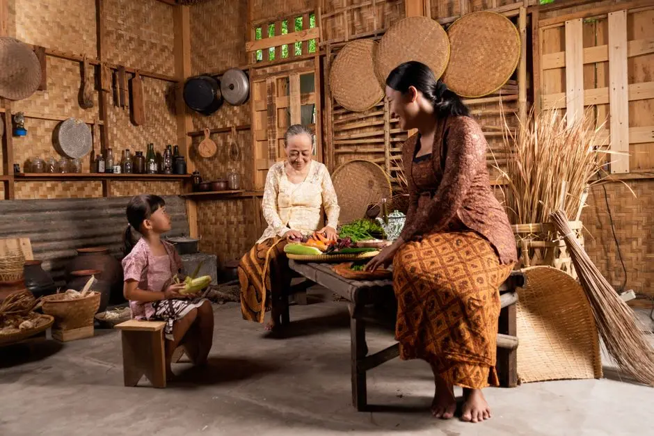 Seorang perempuan paruh baya sedang menganyam tikar dari daun pandan di serambi rumah kayu